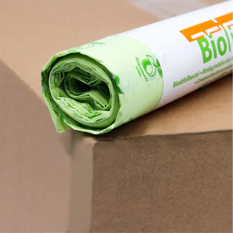 Eine Rolle hellgrüner DEISS Biomüllbeutel 30 Liter, 06030, die zu 100% kompostierbar sind, liegt auf einem braunen Karton. Die Verpackung ist teilweise sichtbar und zeigt ein umweltfreundliches Logo und den Schriftzug „Bio“ in fetten orangefarbenen Buchstaben der EMIL DEISS KG (GmbH + Co.).