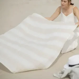 Linen Huckaback Beach Towel in white natural striped, being spread out on the beach